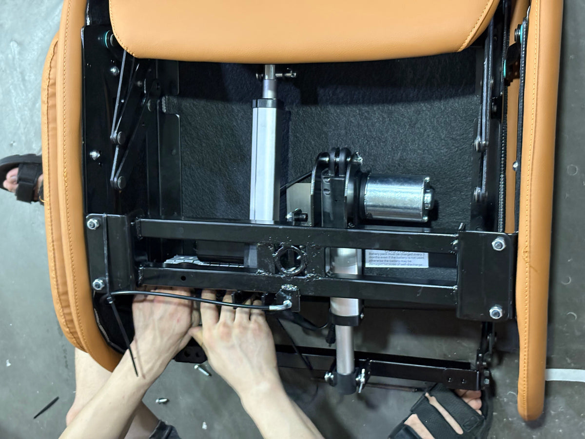A close-up of a person's hands adjusting the black metal frame and mechanism of an office chair with tan leather upholstery, viewed from underneath.