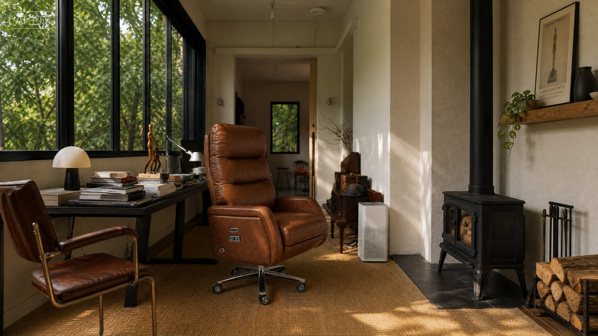 A warm brown leather office chair with a five-star swivel base is positioned in a sunlit home office interior next to a desk and large windows.